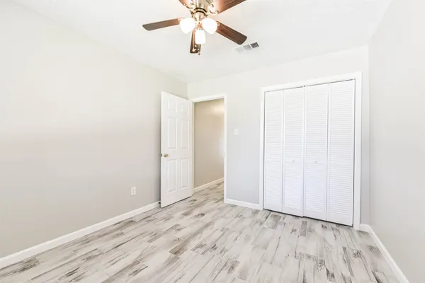 an empty room with wooden floor fan and windows