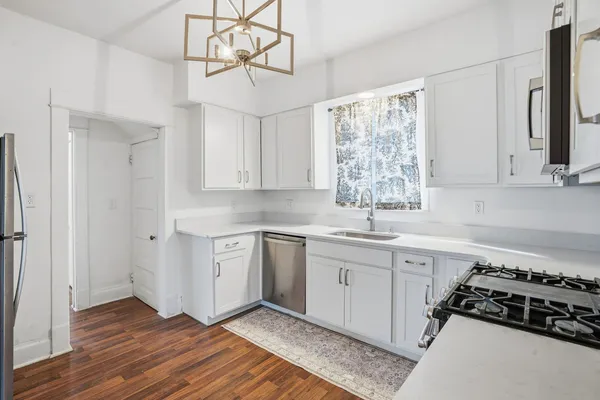 a kitchen with stainless steel appliances a stove a sink and white cabinets with wooden floor