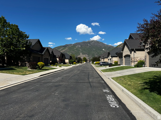 1154 Sunset Dunes Way Draper, UT 84020 - Photo 7 of 50 Residential street with a mountain backdrop, lined with homes featuring stone and stucco exteriors, dark shingled roofs, and attached garages