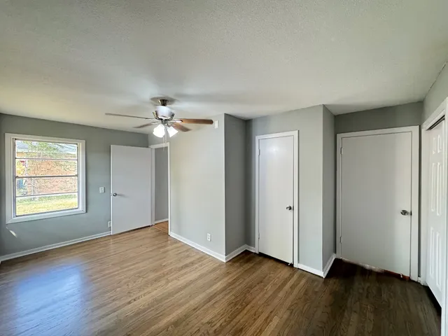 an empty room with wooden floor chandelier fan and windows