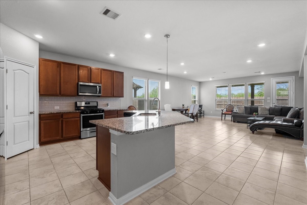2320 Rosemary Street Rosenberg, TX 77469 - Photo 11 of 40 This open-concept living area features a modern kitchen with stainless steel appliances, a central island, and ample cabinetry. The space includes a dining area and a cozy living room with large windows, providing plenty of natural light and a view of the backyard.