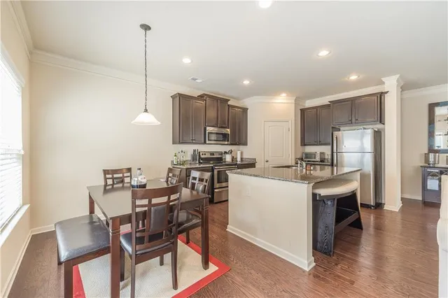a kitchen with stainless steel appliances kitchen island granite countertop a table chairs and a refrigerator