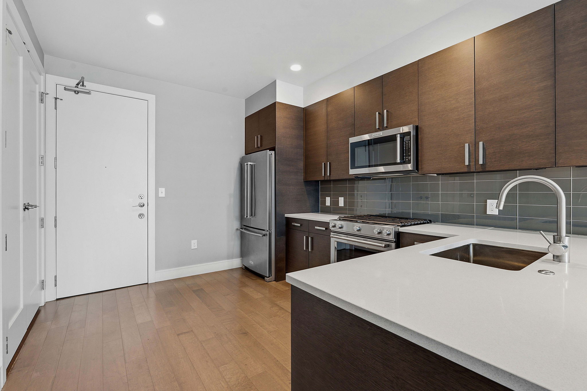 222 West Avenue, Unit 2207 Austin, TX 78701 - Photo 5 of 30 Kitchen featuring wood-finish flooring, dark wood cabinetry, stainless steel appliances, and light-toned countertops