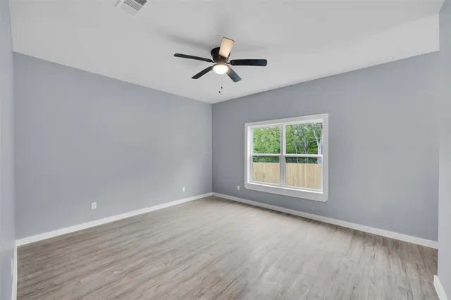 an empty room with wooden floor ceiling fan and windows