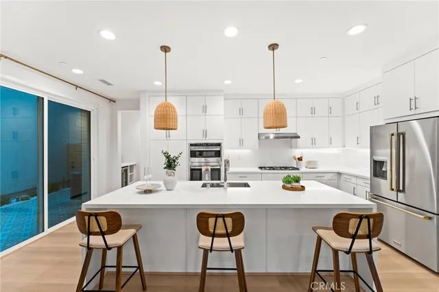 a kitchen with stainless steel appliances kitchen island granite countertop a sink a stove a refrigerator and white cabinets with wooden floor