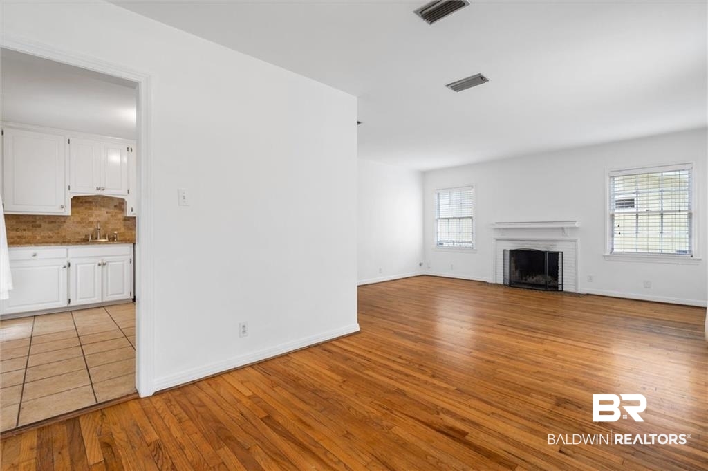 218 Grand Boulevard Mobile, AL 36607 - Photo 20 of 22 Unfurnished living room featuring sink, a fireplace, a healthy amount of sunlight, and light hardwood / wood-style flooring