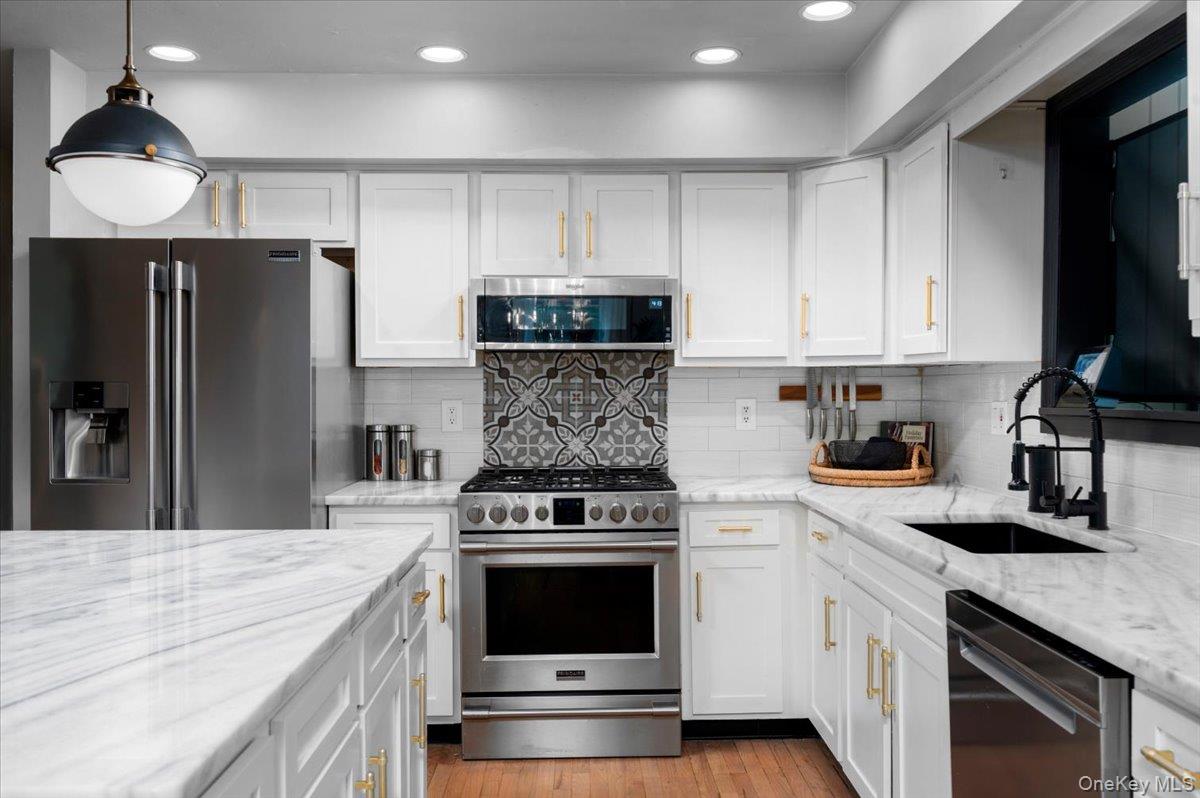 13 Jacks Pond Road Newburgh, NY 12550 - Photo 10 of 44 Kitchen featuring white cabinetry with gold-finish hardware, stainless steel appliances, and warm wood-finish flooring.