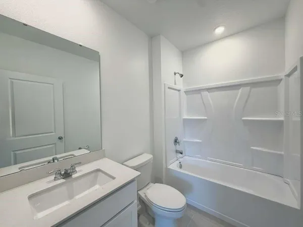 a bathroom with a bathtub shower sink vanity mirror and toilet