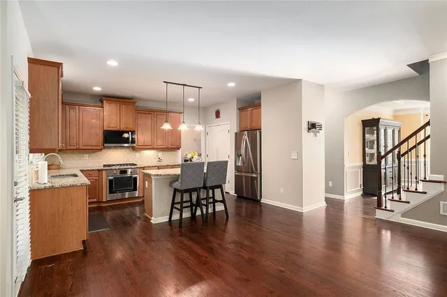 a kitchen with stainless steel appliances kitchen island granite countertop a stove top oven a sink a refrigerator with a dining table and chairs with wooden floor