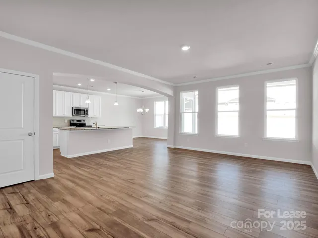 a view of an empty room with kitchen and window