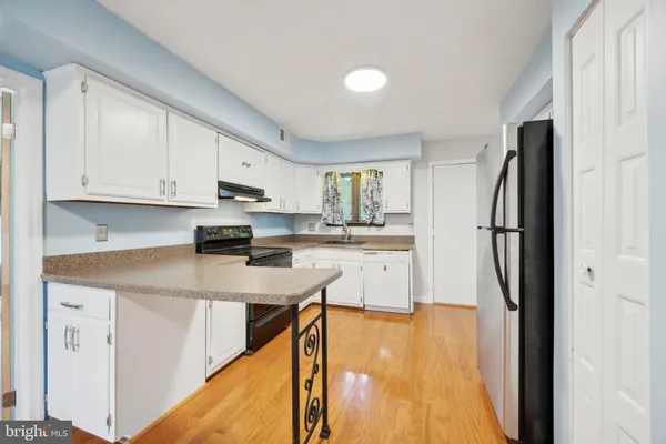 a kitchen with stainless steel appliances granite countertop a refrigerator a sink dishwasher a stove and white cabinets with wooden floor
