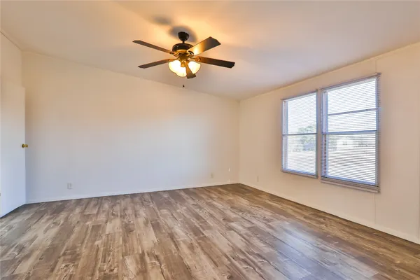 an empty room with wooden floor fan and windows