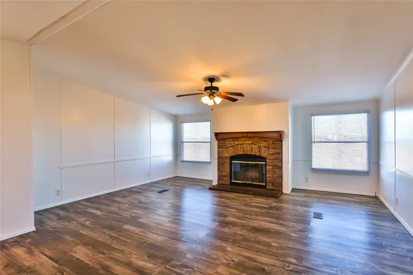 an empty room with wooden floor fireplace and windows