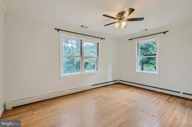an empty room with wooden floor chandelier fan and windows