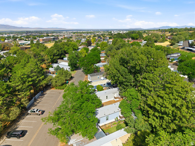 2875 North Hill Field Road, Unit 62 Layton, UT 84041 - Photo 29 of 34 Aerial panorama showcasing a residential development nestled among established trees, with a distant city skyline and mountain ranges under a clear sky