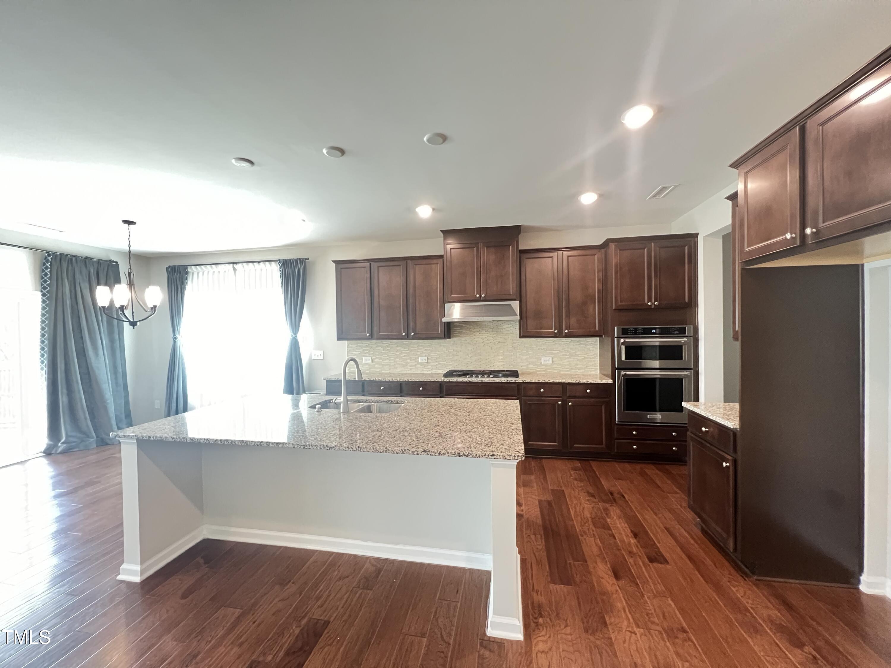 3385 Lovage Drive Apex, NC 27502 - Photo 3 of 19 a large kitchen with kitchen island a stove a refrigerator a sink and dishwasher with wooden floor
