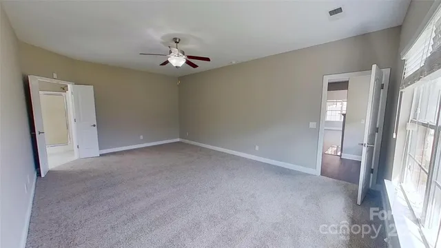 an empty room with chandelier fan and windows