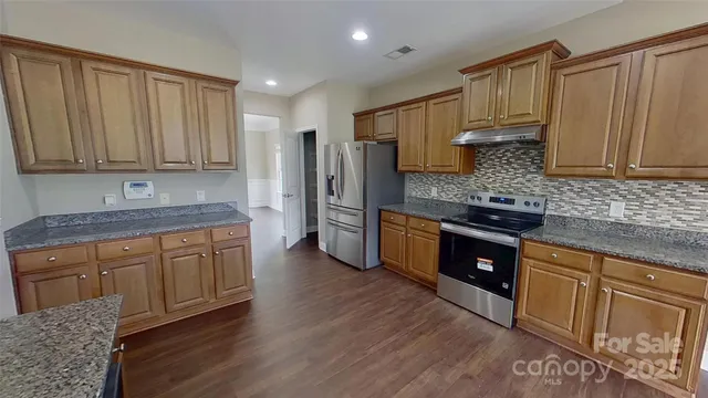 a kitchen with stainless steel appliances granite countertop a stove a sink dishwasher and a refrigerator with wooden cabinets