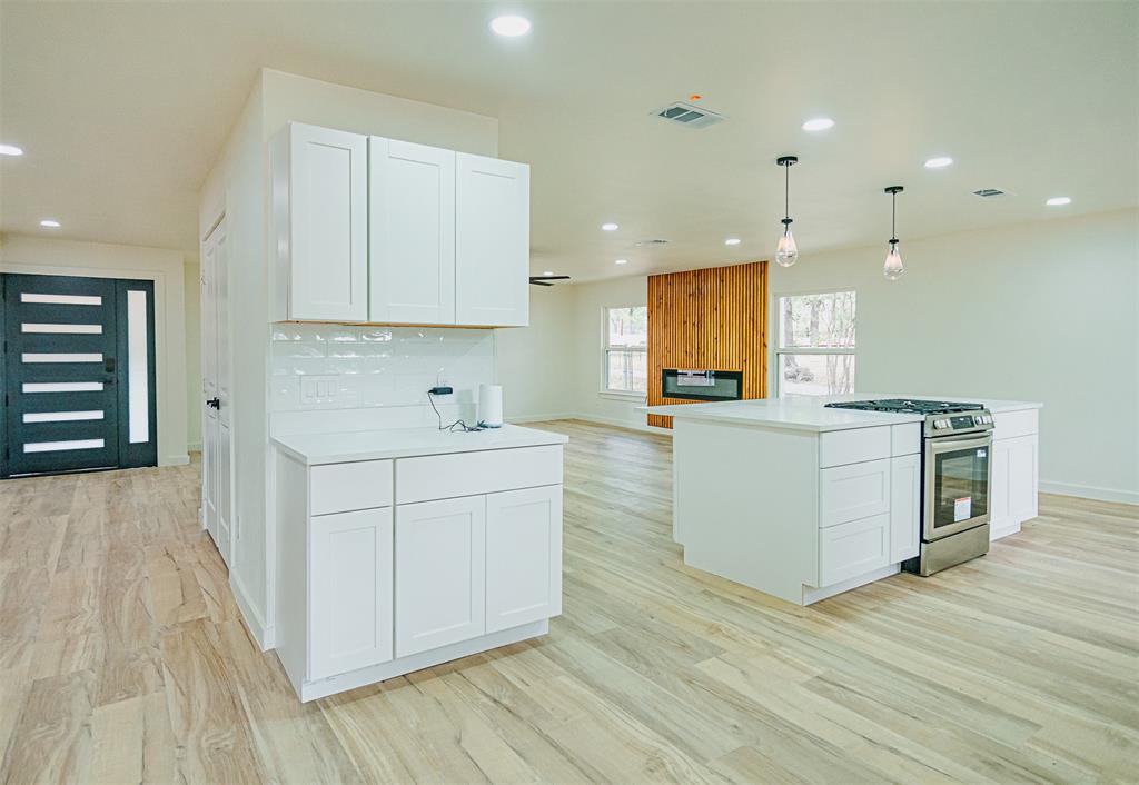 1832 Johnson Road Keller, TX 76248 - Photo 10 of 25 Open-concept layout with wood-finish flooring, white cabinetry, a built-in stainless steel range/oven, and a fireplace with a wood-paneled surround