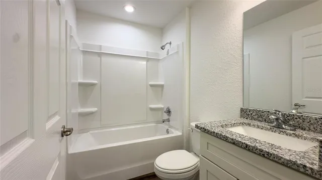 a bathroom with a granite countertop bathtub shower sink vanity and toilet