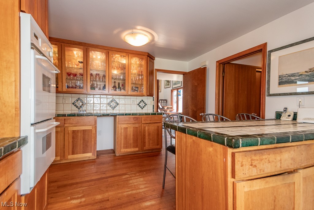 7563 Salida Road Mentor, OH 44060 - Photo 8 of 48 Kitchen with white double oven, tile countertops, wood finished floors, decorative backsplash, and a kitchen breakfast bar