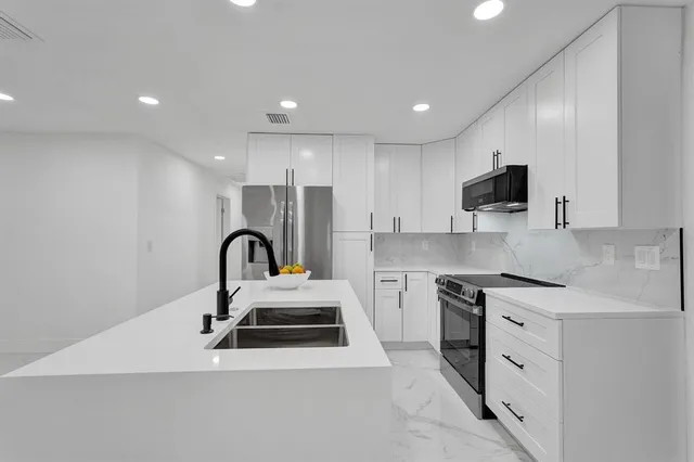 a kitchen with stainless steel appliances a sink a stove a microwave a sink a refrigerator and white cabinets with wooden floor