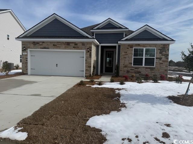 Craftsman-style house with a garage, stone siding, and driveway