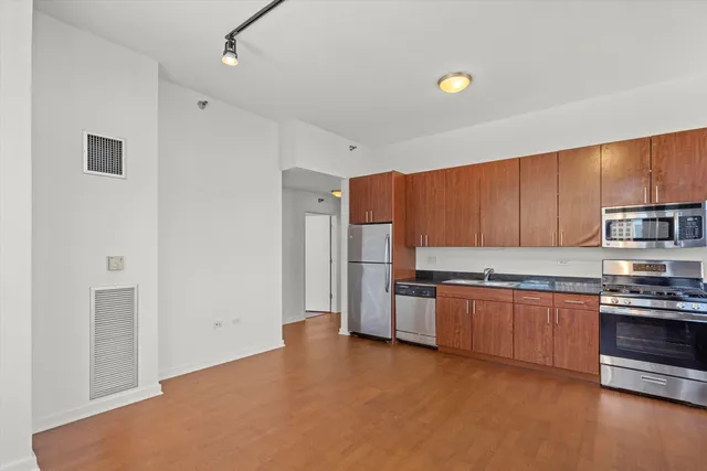 a kitchen with stainless steel appliances granite countertop a stove top oven a sink dishwasher and a refrigerator with wooden floor