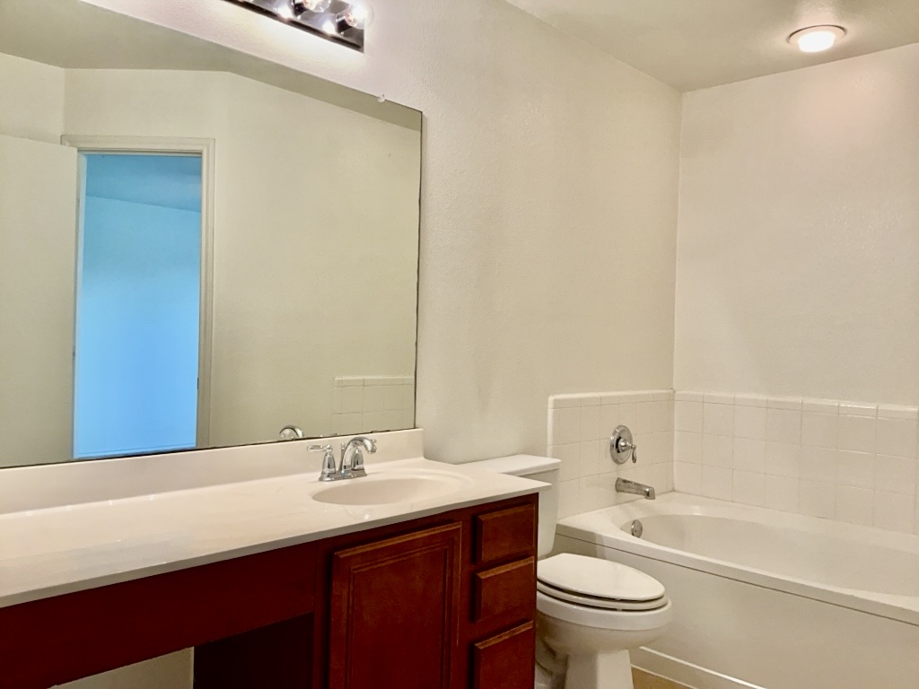 2242 Perkins Place Georgetown, TX 78626 - Photo 13 of 25 Bathroom featuring a built-in vanity with a white countertop and integrated sink, a large wall-mounted mirror, and a white tiled bathtub with chrome fixtures