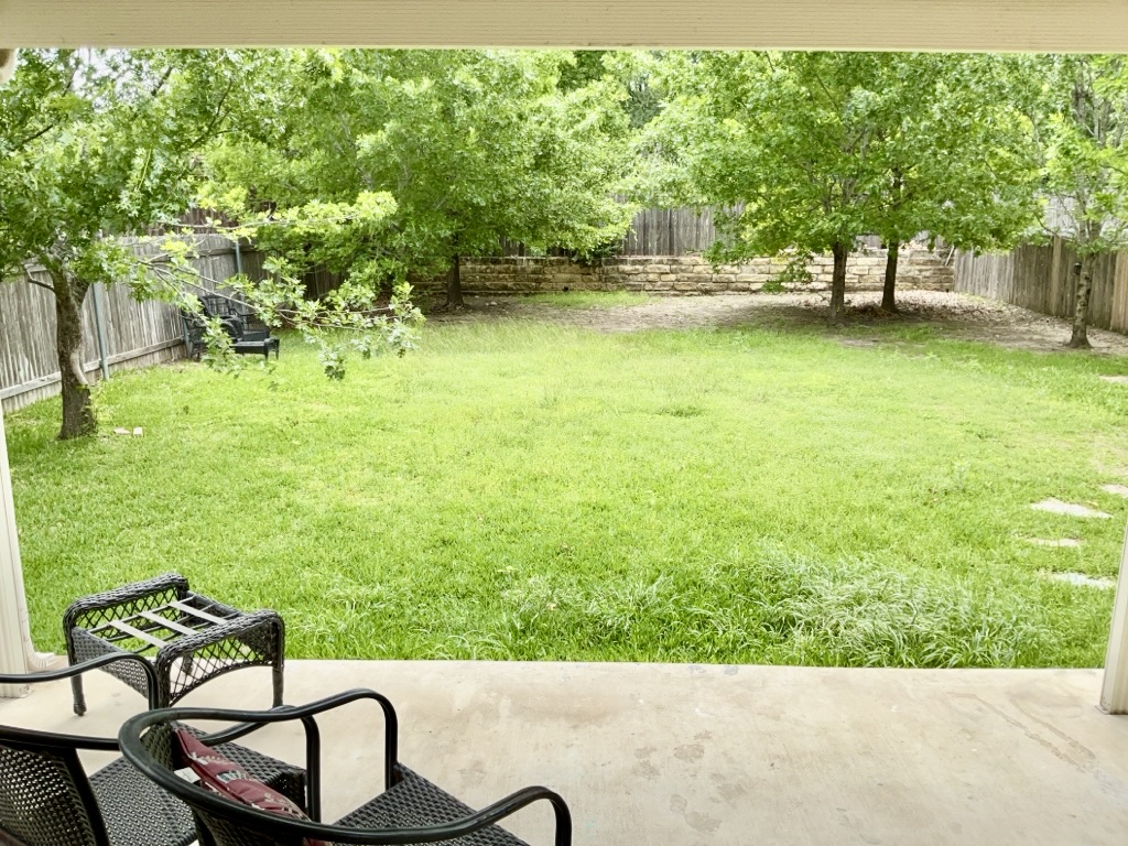 2242 Perkins Place Georgetown, TX 78626 - Photo 24 of 25 Expansive backyard with a green lawn, mature trees, wood privacy fencing, and a stone retaining wall