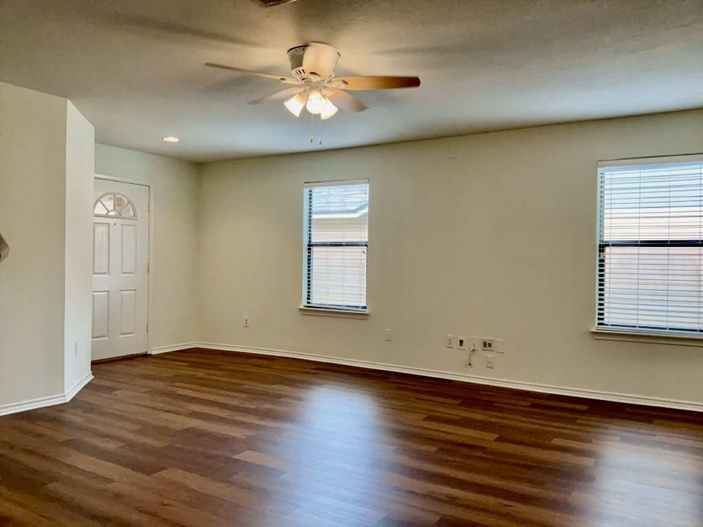 2242 Perkins Place Georgetown, TX 78626 - Photo 5 of 25 Spacious interior room with wood-finish flooring, two large windows with blinds, a ceiling fan with integrated lighting, and a white paneled entry door with an arched glass insert