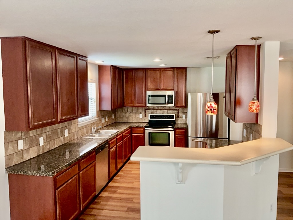 2242 Perkins Place Georgetown, TX 78626 - Photo 6 of 25 U-shaped kitchen with wood-finish flooring, dark wood cabinetry, and a granite-patterned countertop