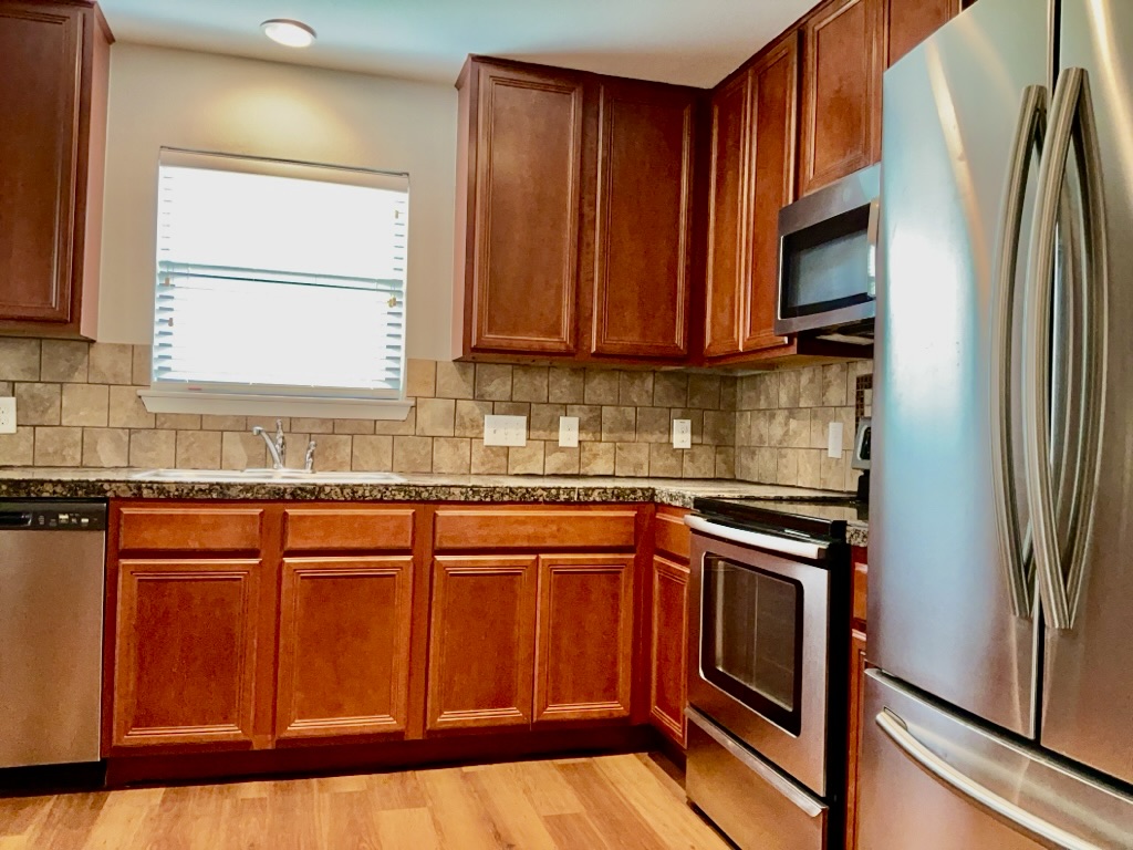 2242 Perkins Place Georgetown, TX 78626 - Photo 8 of 25 Kitchen featuring wood-finish flooring, dark wood cabinetry, a mosaic tile backsplash, and stainless steel appliances including a refrigerator, dishwasher, and range