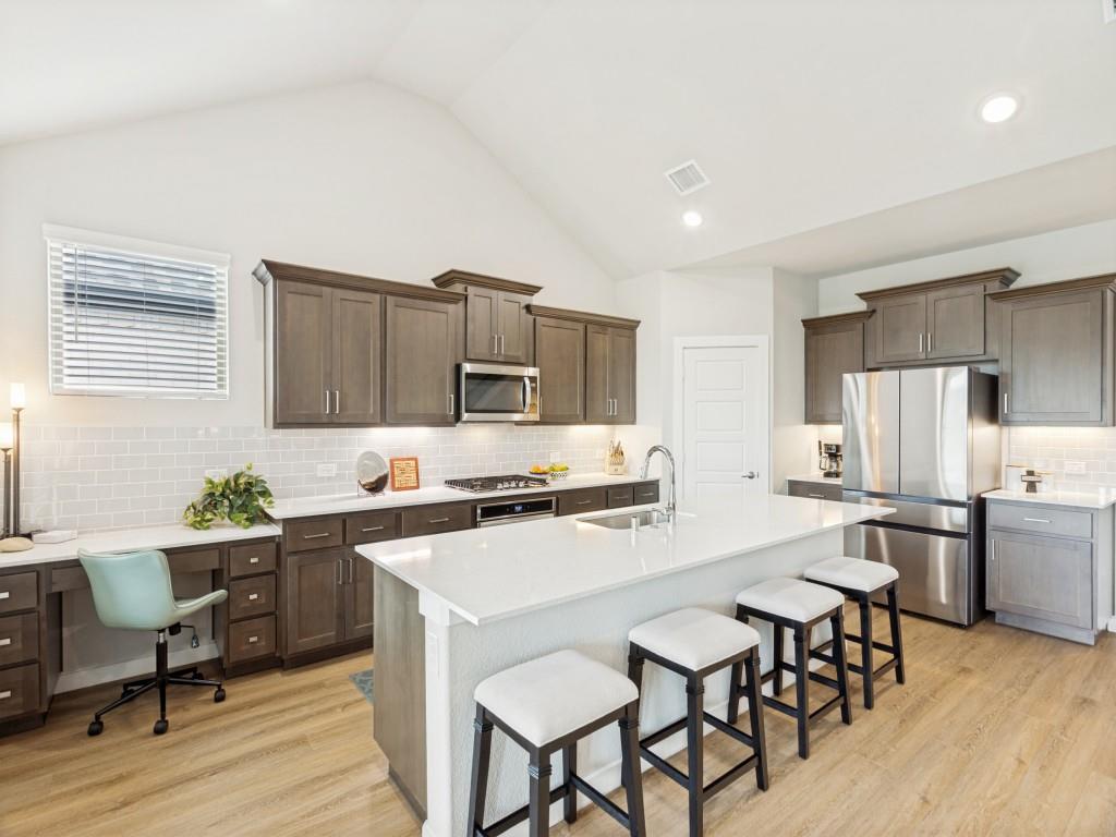 10613 Smiths Bnd Road Fort Worth, TX 76126 - Photo 6 of 29 Open-concept kitchen featuring an expansive central island with seating, wood-finish flooring, dark wood cabinetry, stainless steel appliances, and a tiled backsplash