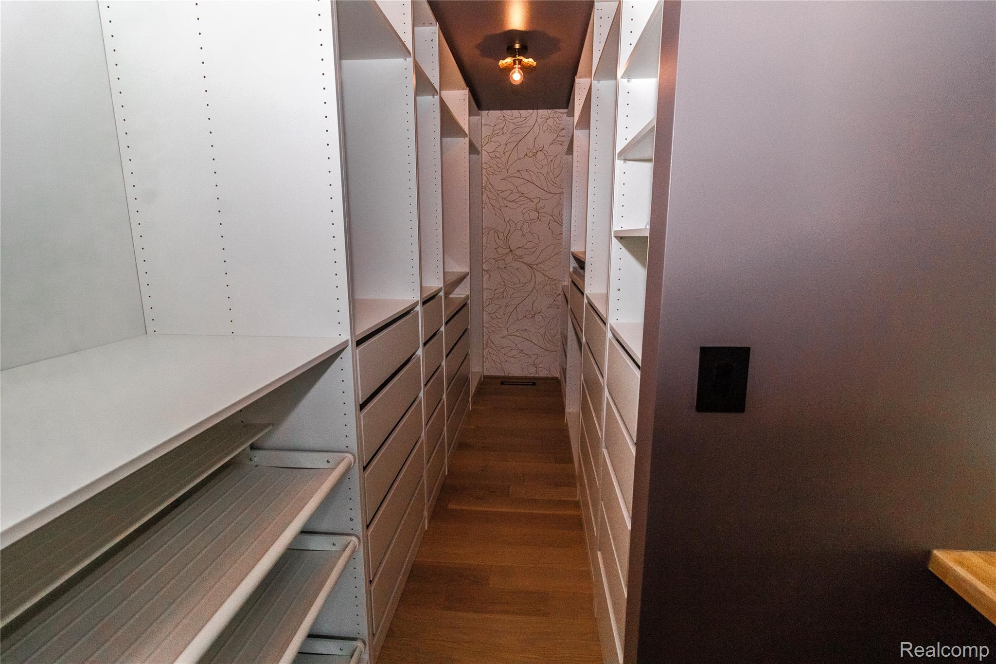 1138 Baldwin Road Lapeer, MI 48446 - Photo 18 of 49 Walk-through closet featuring built-in white shelving, integrated drawers, wood-finish flooring, and a decorative ceiling light fixture