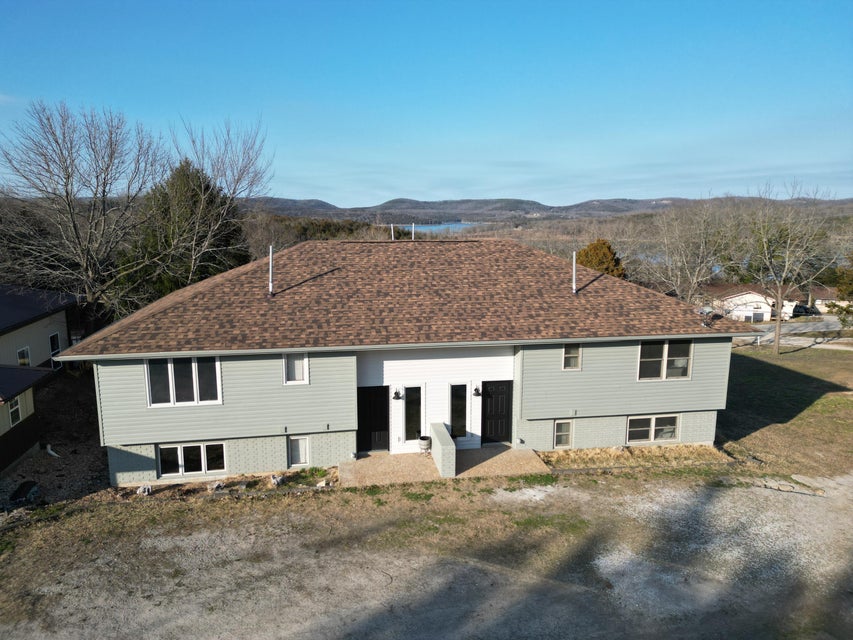 Duplex property featuring light blue siding with white trim, a brown shingle roof, and a partial brick foundation