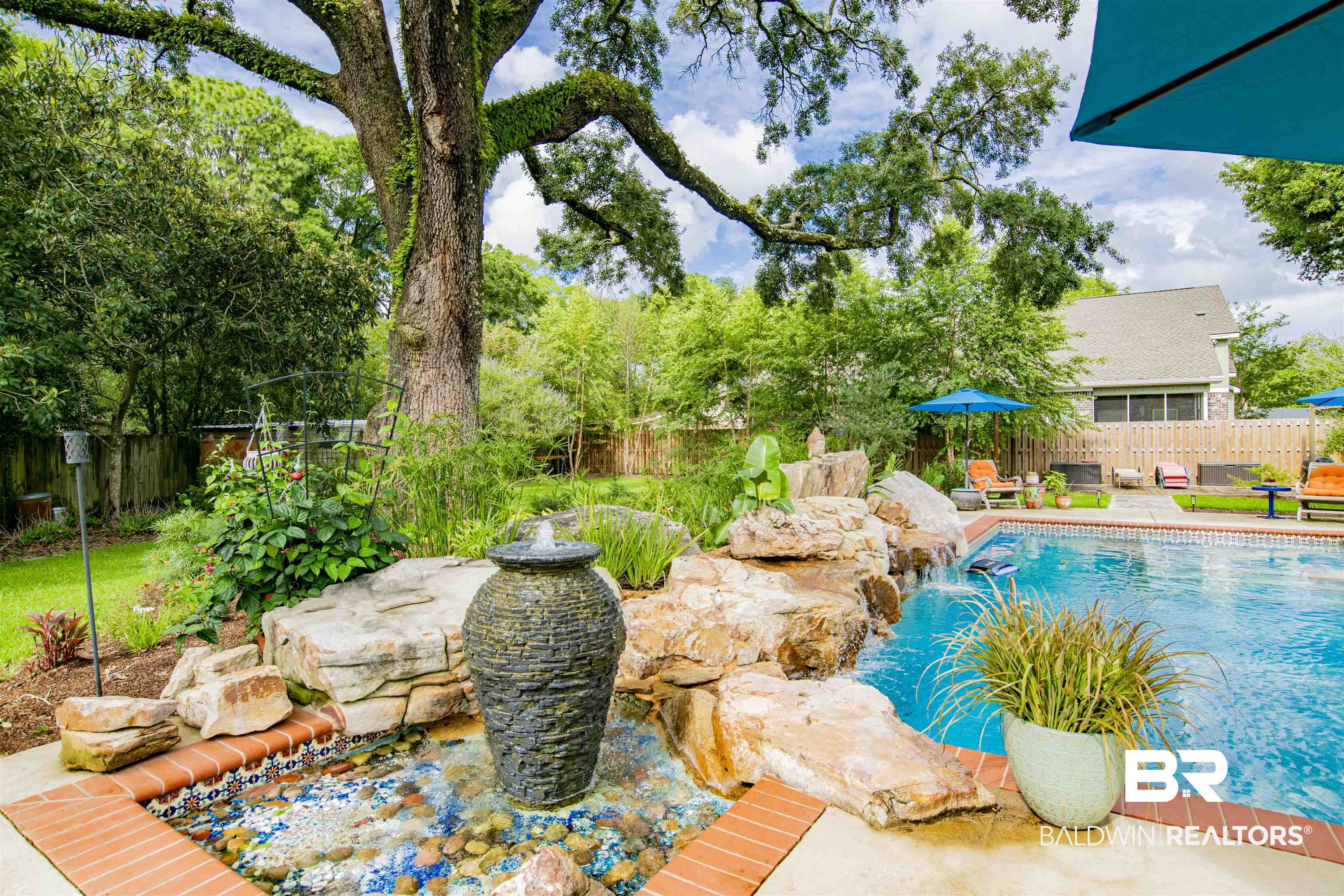 809 Bernard Circle Mobile, AL 36693 - Photo 64 of 75 Backyard oasis featuring a swimming pool with rock waterfall, adjacent fountain with decorative basin, mature tree providing natural shade, and lush perimeter landscaping