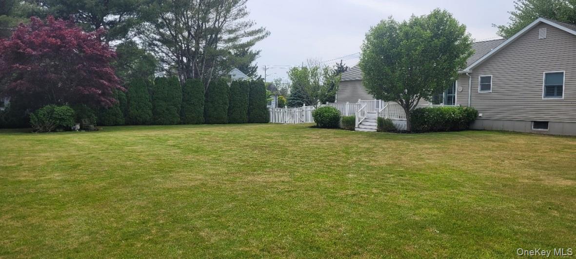 312 Riley Avenue Calverton, NY 11933 - Photo 26 of 30 Expansive green lawn featuring a white privacy fence, mature perimeter trees, and a multi-level deck with white railings