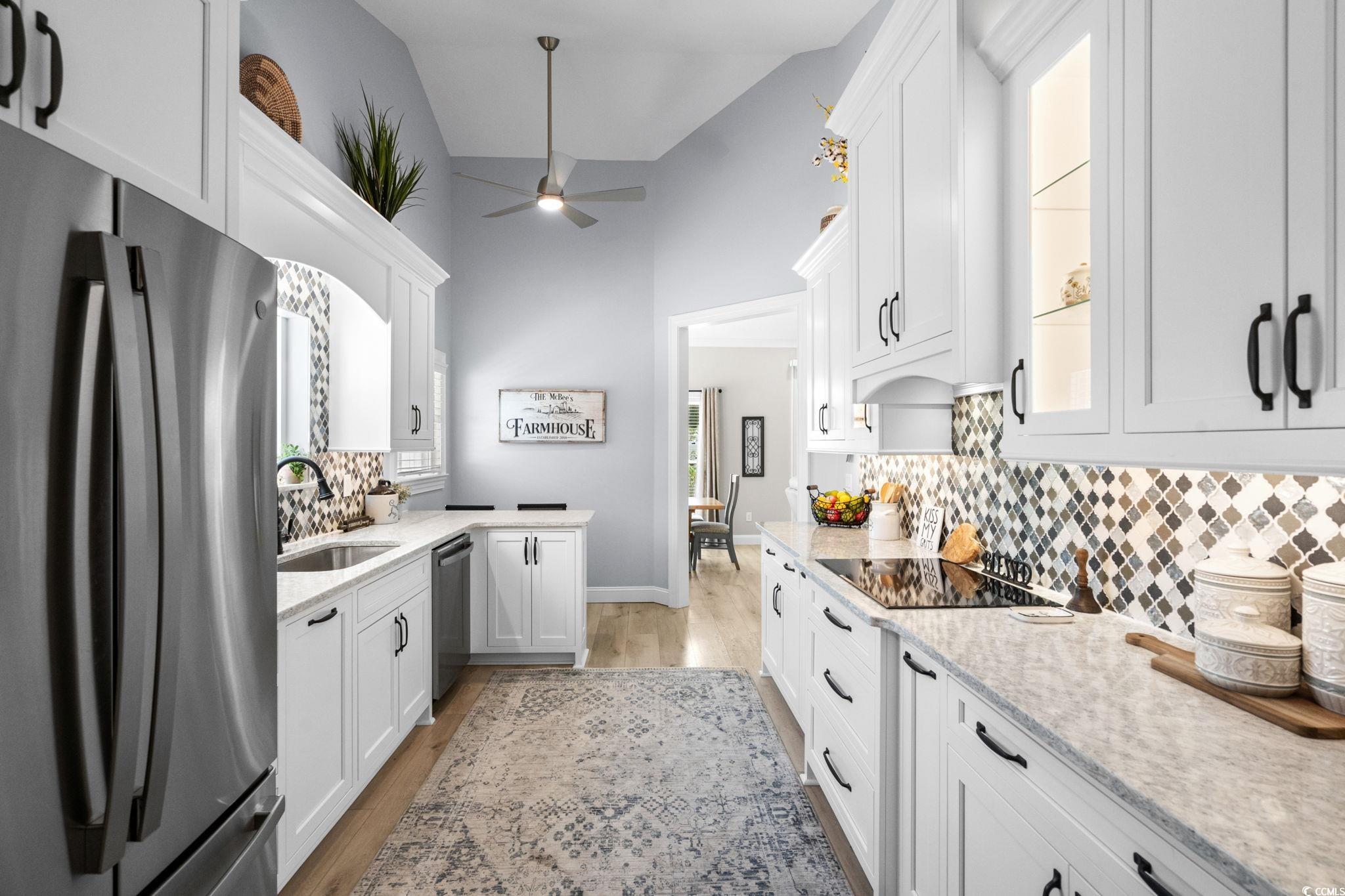408 Highland Ridge Drive Myrtle Beach, SC 29588 - Photo 13 of 39 Kitchen with appliances with stainless steel finishes, decorative backsplash, white cabinetry, light wood-style floors, and high vaulted ceiling