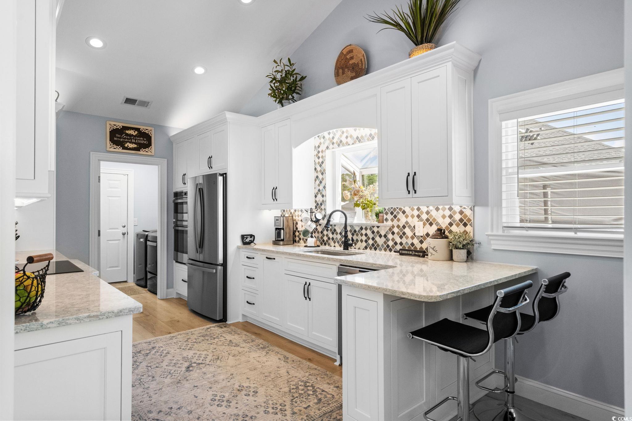 408 Highland Ridge Drive Myrtle Beach, SC 29588 - Photo 10 of 39 Kitchen with white cabinetry, light wood-style floors, decorative backsplash, GE Profile stainless steel appliances, and a peninsula