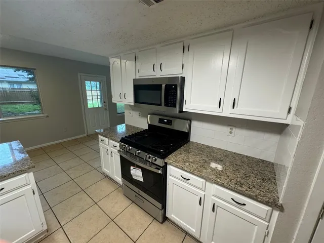 a kitchen with granite countertop a stove top oven microwave and cabinets