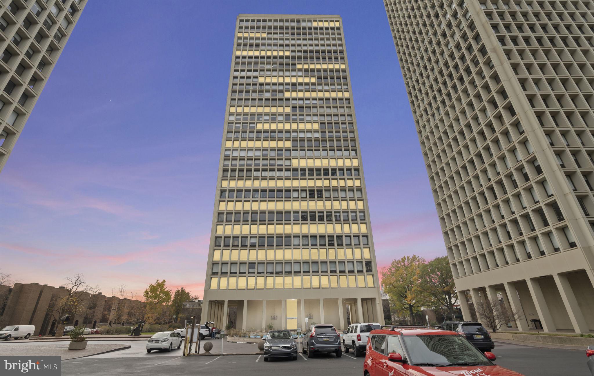 a front view of a building with lot of cars and trees