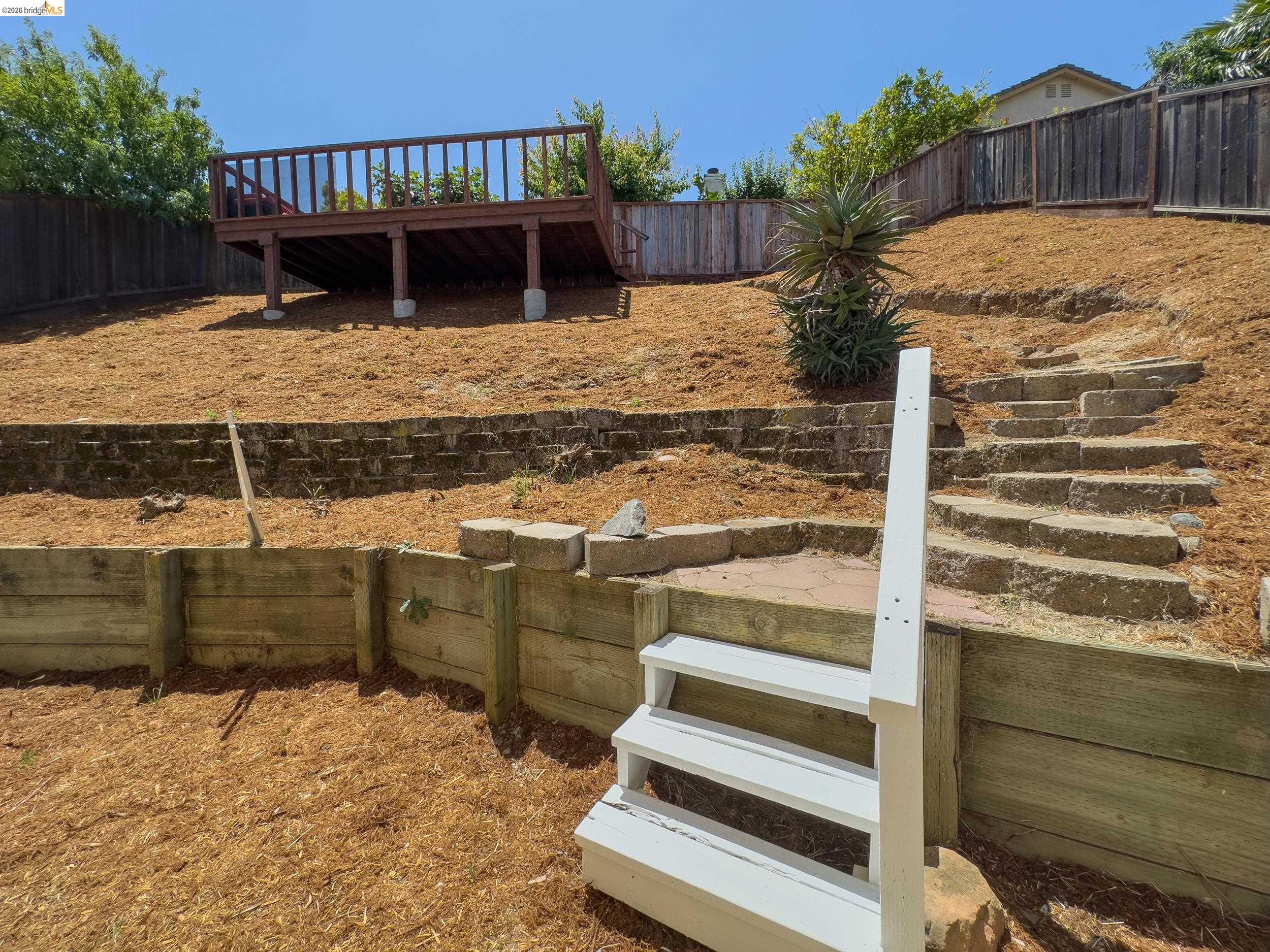 512 Burdick Drive Bay Point, CA 94565 - Photo 38 of 50 Multi-tiered backyard featuring a high-level deck with wood railing, retaining walls, stone steps, and a white wooden staircase