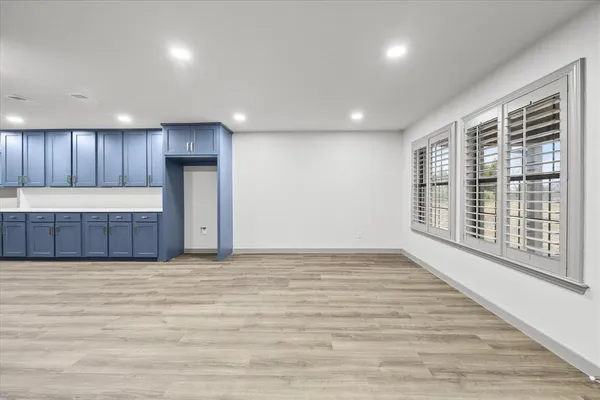 a view of an empty room with wooden floor and a kitchen