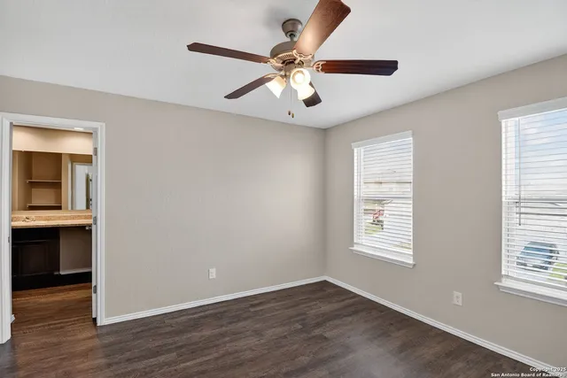 an empty room with wooden floor chandelier fan and windows