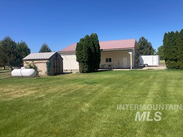 1095 County Road 70 Weiser, ID 83672 - Photo 29 of 44 Expansive lawn area with a detached storage shed, visible propane tank, and a light-colored main structure featuring a red metal roof