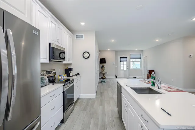 a kitchen with stainless steel appliances kitchen island granite countertop a stove a sink a refrigerator and white cabinets with wooden floor