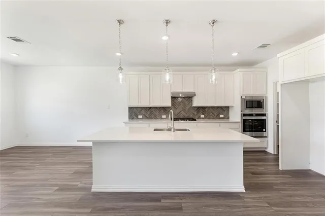 a large kitchen with kitchen island a stove a sink a refrigerator and white cabinets with wooden floor