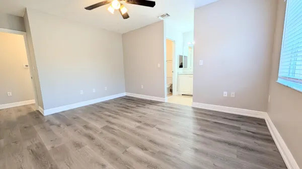 an empty room with wooden floor chandelier fan and windows