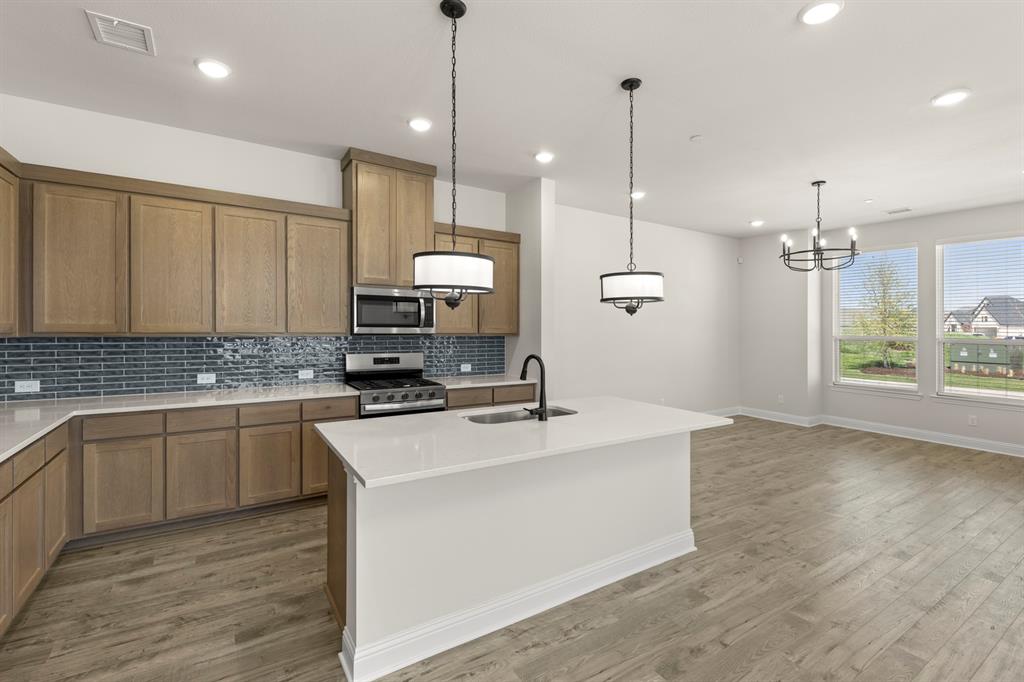3900 Keya Drive Prosper, TX 75078 - Photo 12 of 36 a kitchen with stainless steel appliances granite countertop a sink a stove a refrigerator and white cabinets with wooden floor